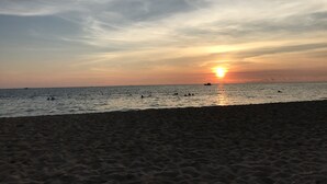 A beach at sunset with the sun low on the horizon, calm sea, and a sandy shore. - Bayya Hotel Phu Quoc (Phu Quoc)