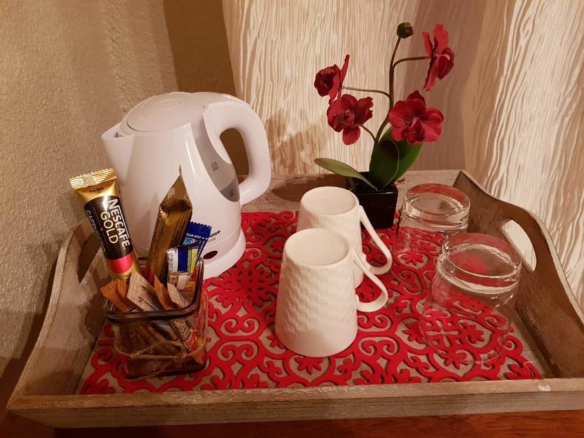 Un plateau avec une cafetière blanche, deux tasses blanches, un petit vase avec des fleurs rouges, un pot et un tube de crème.
