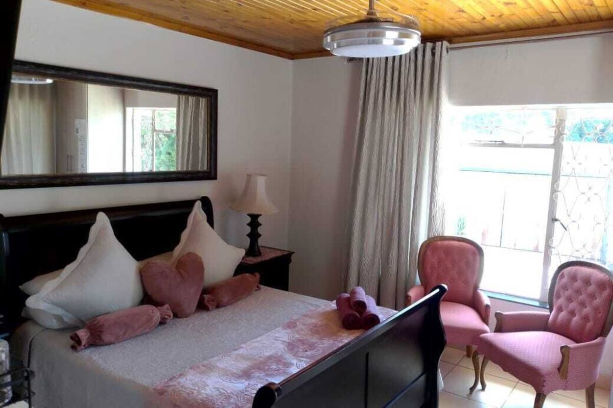 A bedroom with a bed, a chair, a mirror, a lamp, and a window.