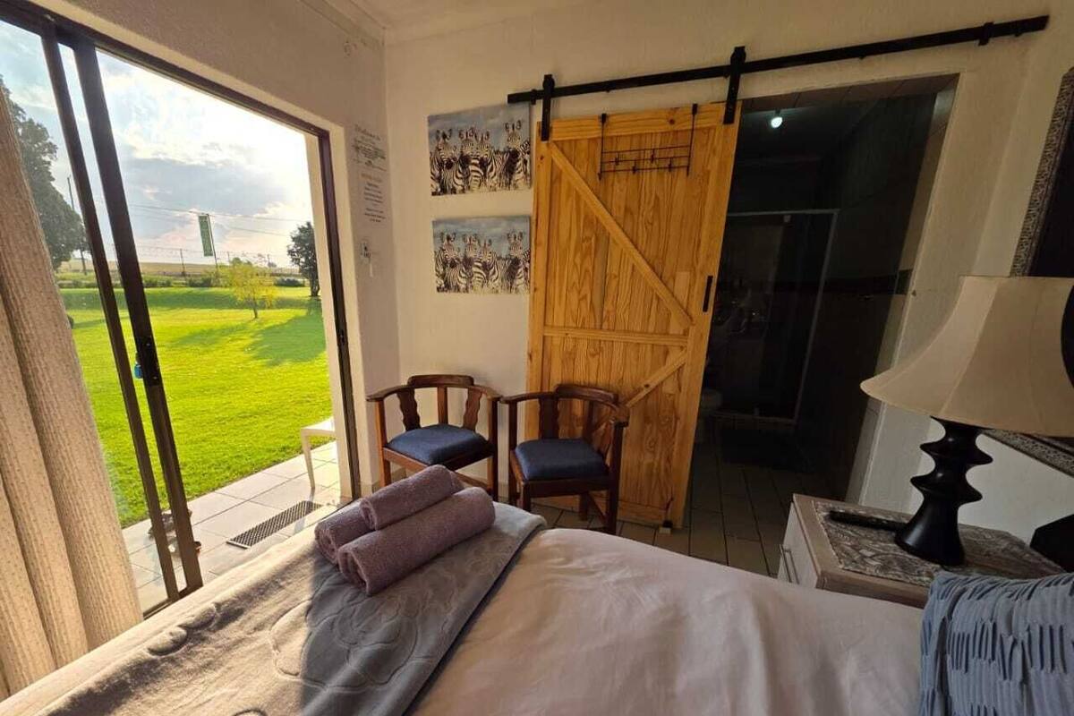 A bedroom with a bed, a chair, a wooden door, and a view of a green field.