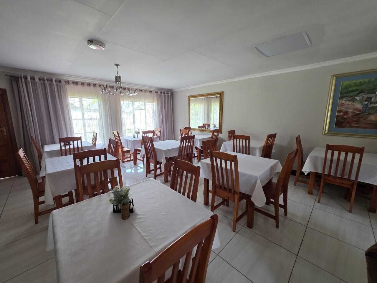 Un espace repas comprenant plusieurs tables et chaises, de grandes fenêtres avec des rideaux et un luminaire au plafond.