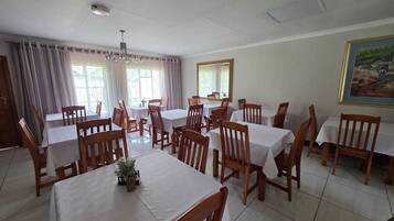 Un espace repas comprenant plusieurs tables et chaises, de grandes fenêtres avec des rideaux et un luminaire au plafond.