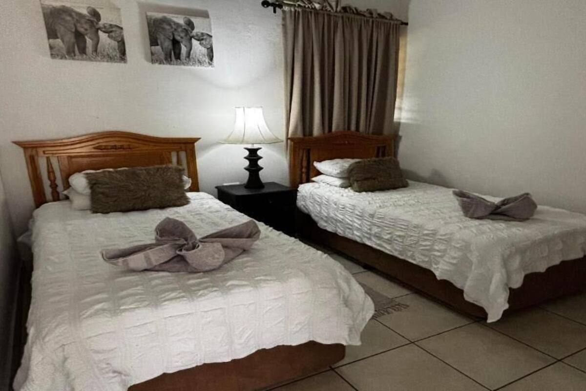 A room with two single beds, a nightstand with a lamp, and a curtain.