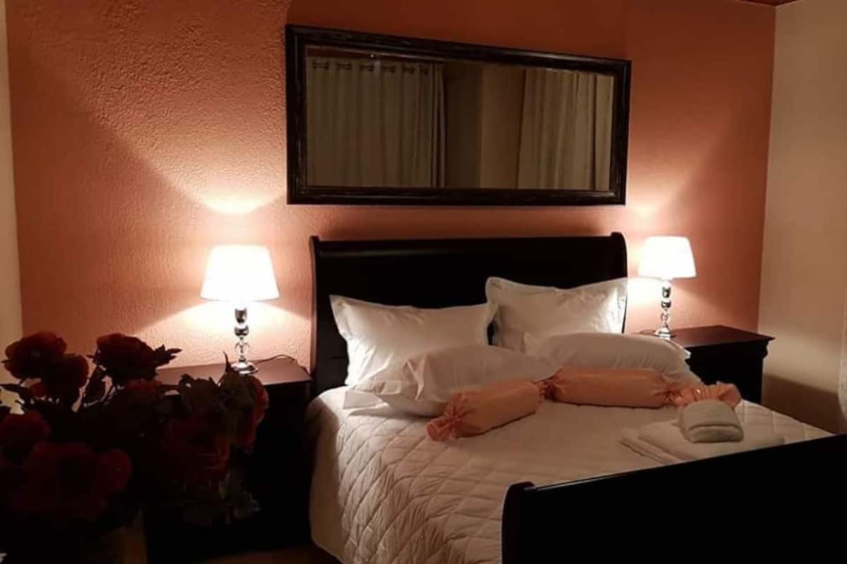 A hotel room with a bed, two bedside lamps, a nightstand with a vase of flowers, and a mirror on the wall.