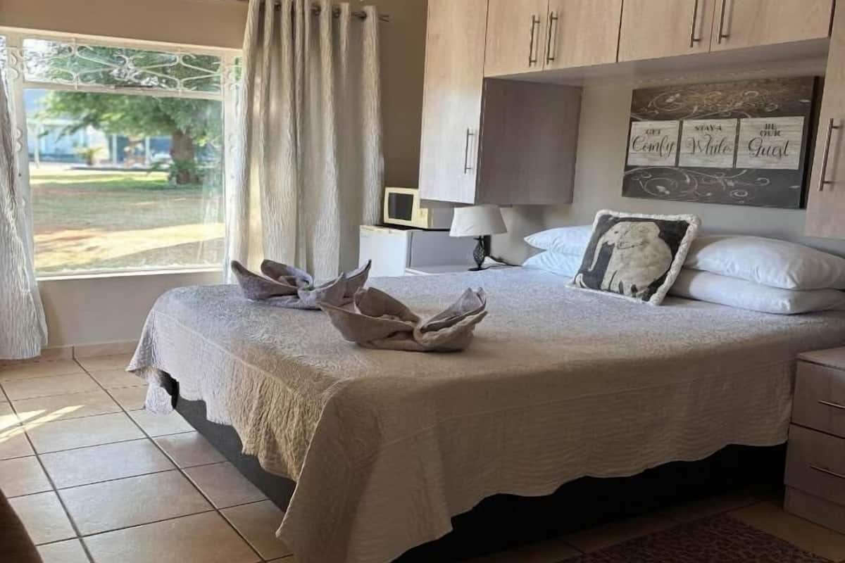 A bedroom with a bed, a desk, a chair, a window with curtains, and a ceiling fan.