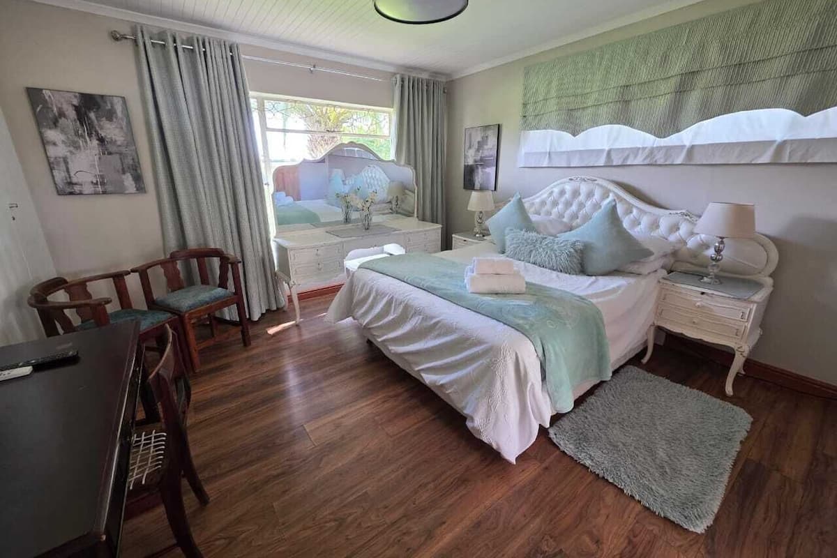 A bedroom with a bed, bedside tables, a desk, chairs, and a window.