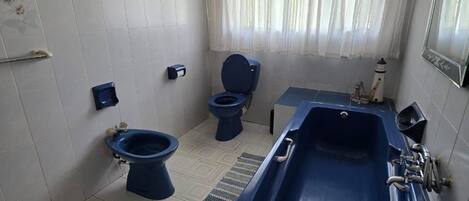 A bathroom with a bathtub, two toilets, a sink, and decorative wall art.