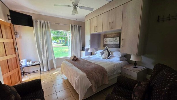 A bedroom with a bed, bedside tables, a ceiling fan, and a view of the outdoors. - Aloe Tree (Krugersdorp)