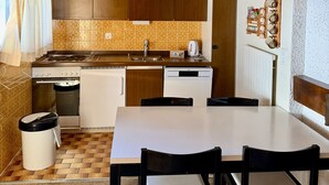 A kitchen with a wooden ceiling, a hanging orange pendant light, a stove, a sink, and a dishwasher. There is a table with chairs and a trash can. - Diablerets D 048 - MOUNTAIN apartment 4 pers (Veysonnaz)