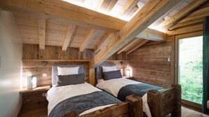 A wooden cabin bedroom with two beds, a skylight, and a window overlooking greenery.