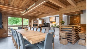 A wooden interior with a large dining table, chairs, and a kitchen area.