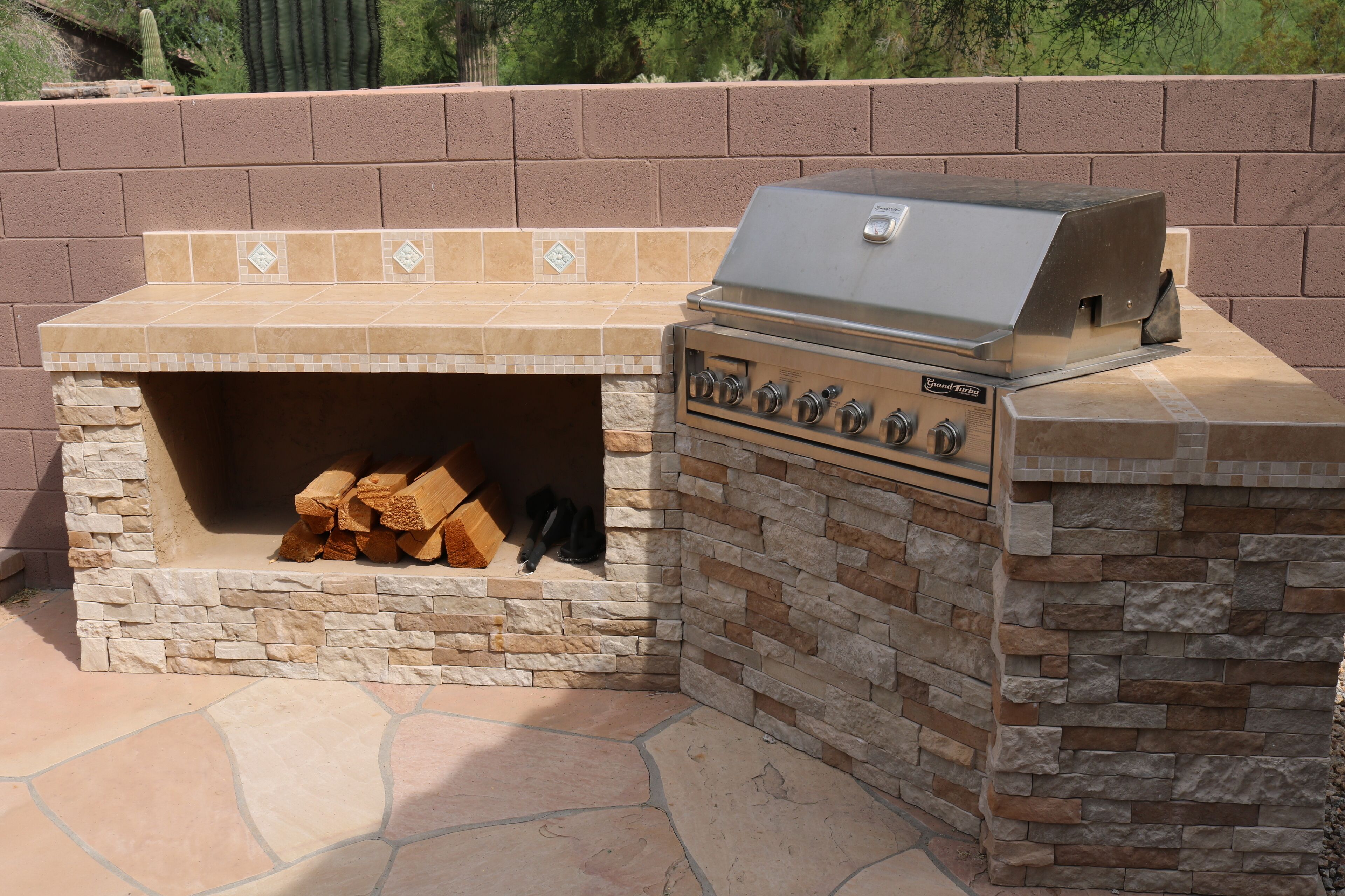 An outdoor barbecue grill with a stone surround and a tiled backsplash.