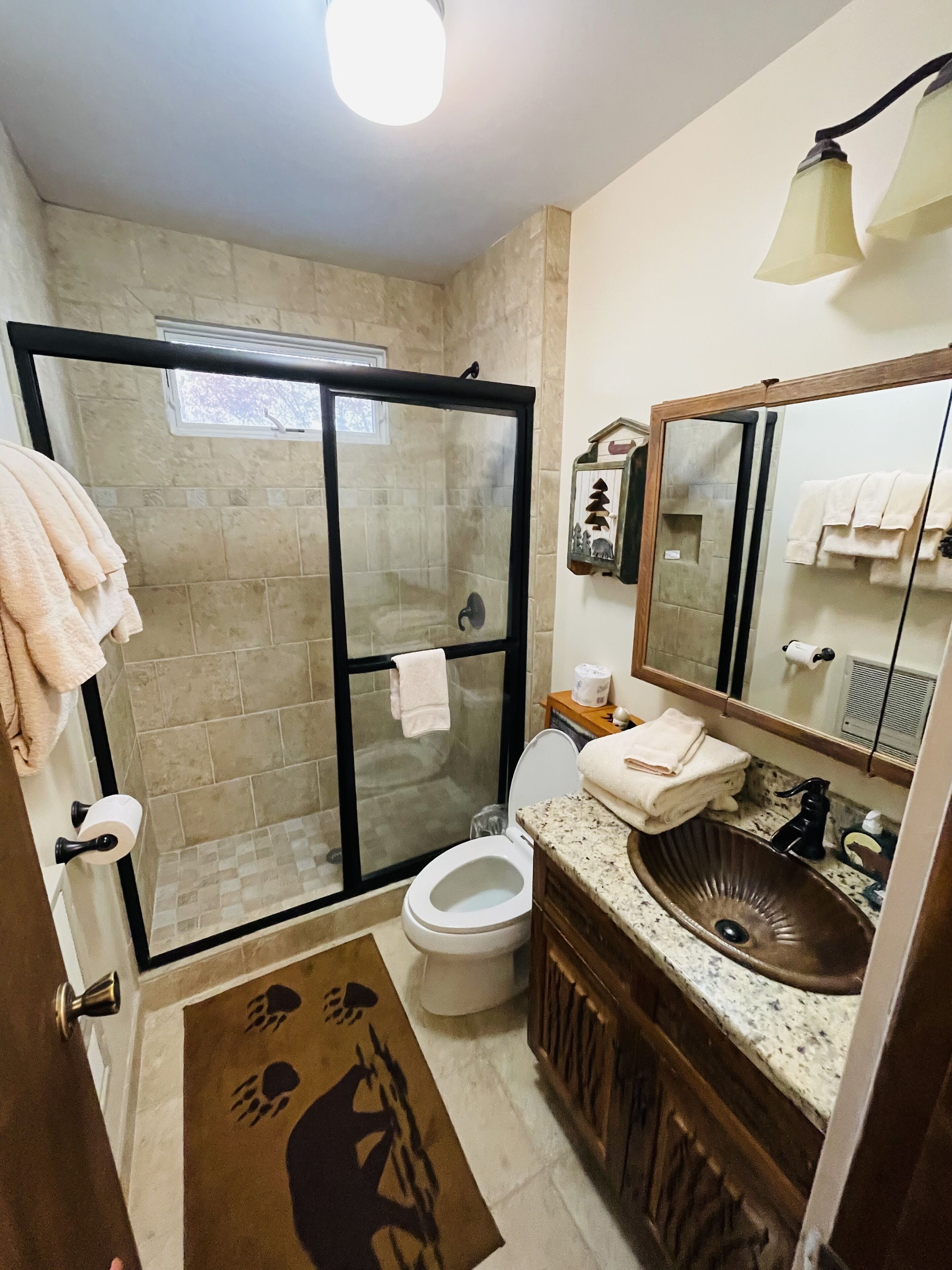 Een badkamer met een douchecabine van glas, een toilet, een wastafel met onderkast en een spiegel.