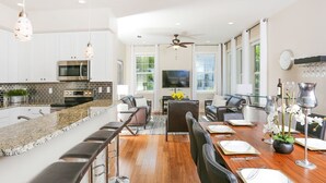 A modern kitchen with a bar area, a dining table set for four, and a television mounted on the wall.