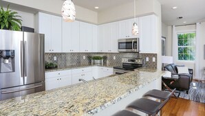 A modern kitchen with granite countertops, stainless steel appliances, and a bar area with stools.