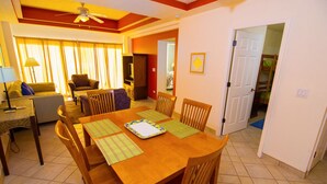 A dining area with a wooden table and chairs, a television in the background, and a door leading to another room. - Beautiful 1½ Bedroom Condo on the Sea of Cortez at Las Palmas Resort D-703A (Puerto Peñasco)
