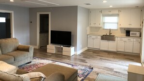 Ein modernes Wohnzimmer mit Flachbildfernseher, einer Couch und einem Couchtisch. Die Küche verfügt über weiße Schränke, eine Mikrowelle und ein Spülbecken.