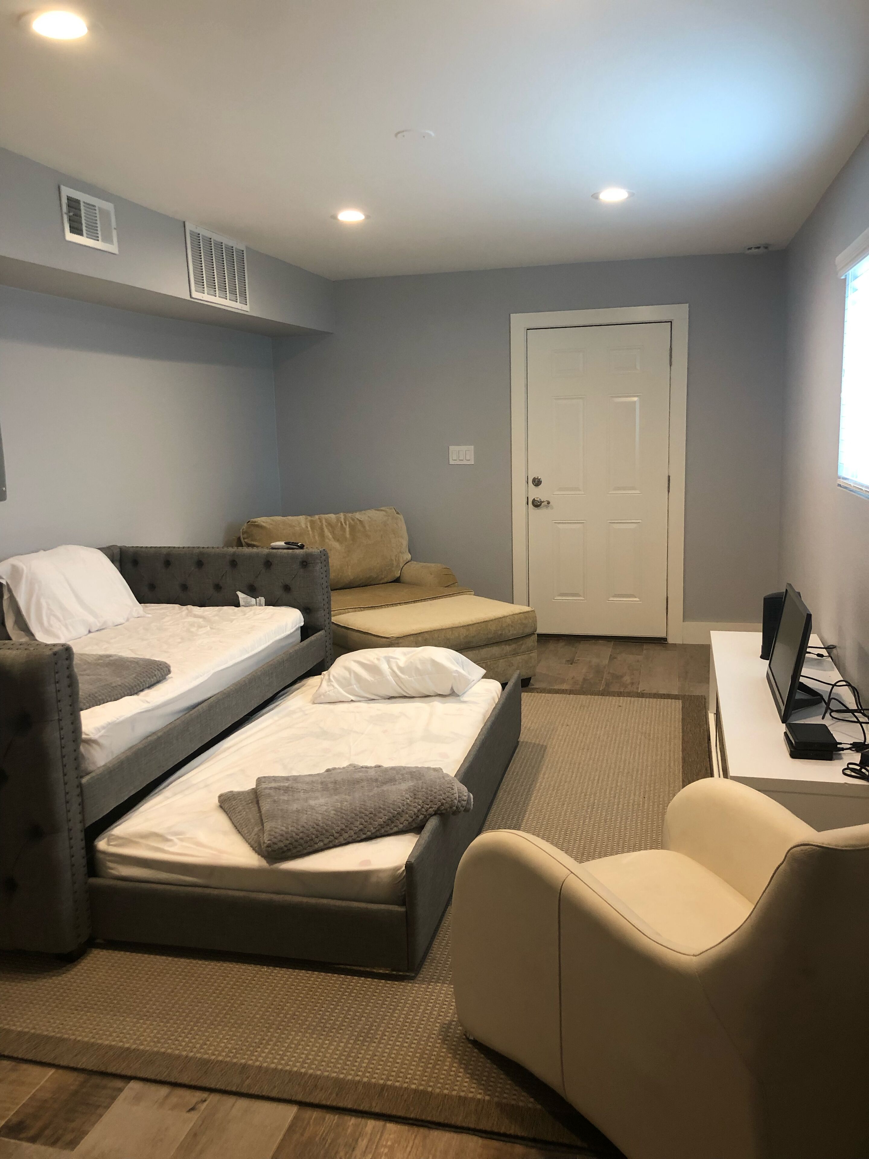 A bedroom with a bed, two chairs, a desk with a computer, and a door.