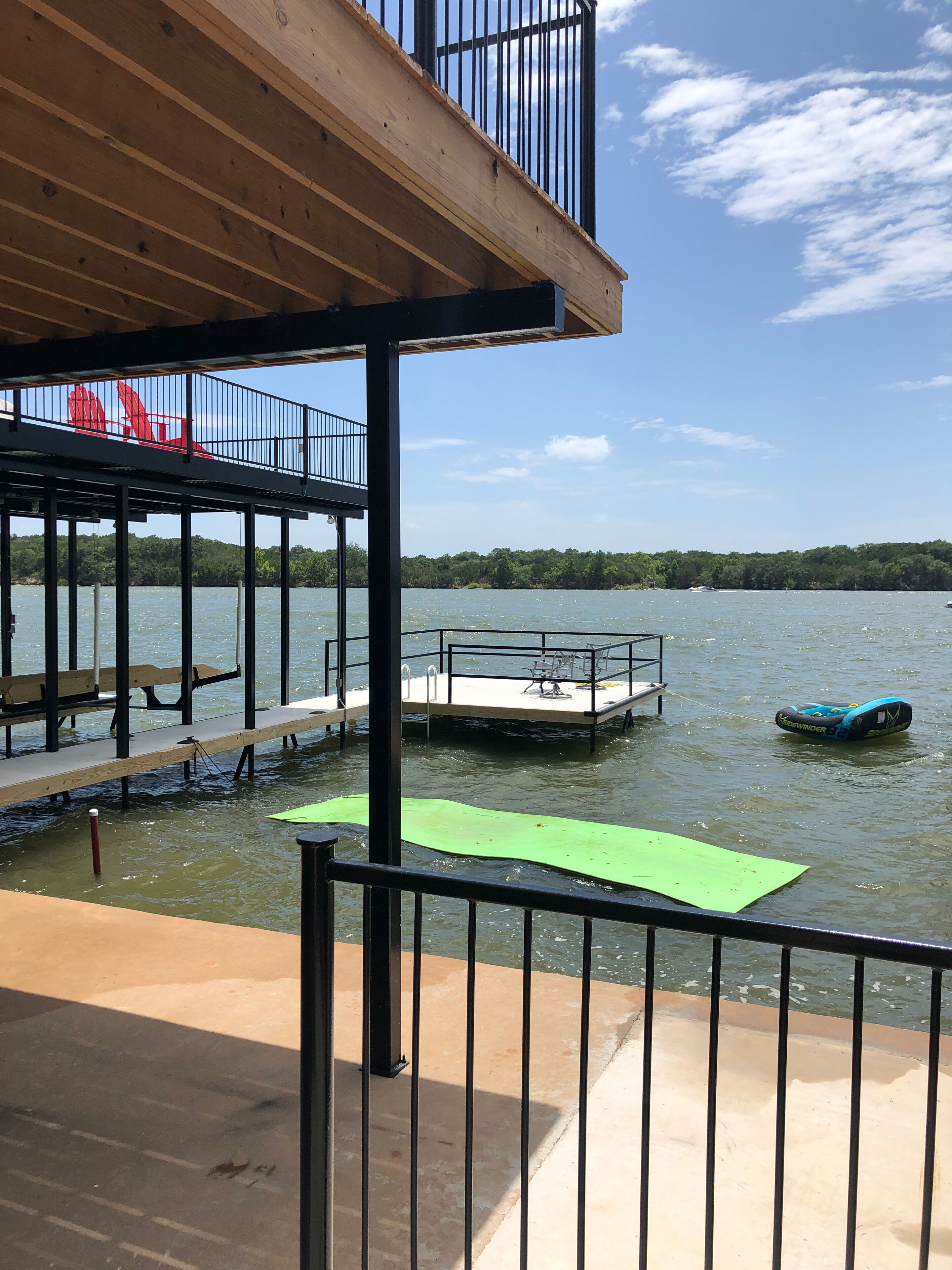 A wooden deck with a railing, a floating dock, and a kayak on the water.