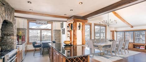 A spacious kitchen with a stone accent wall, a large island with a wine rack, and a dining area with a view of the mountains.