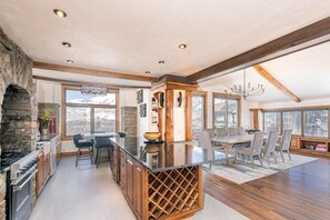 A spacious kitchen with a stone accent wall, a large island with a wine rack, and a dining area with a view of the mountains.