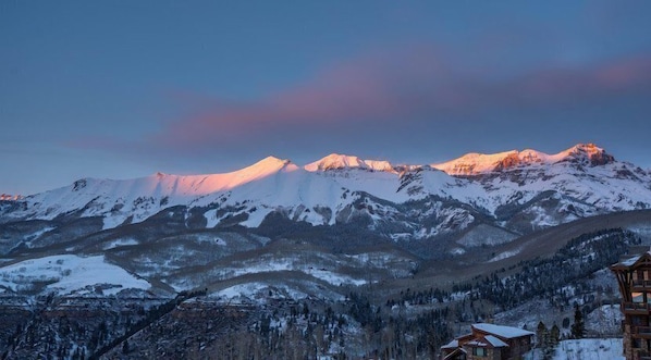 Un paysage de montagne avec des sommets enneigés et un chalet en bois au premier plan.