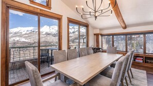 A dining area with a large table and chairs, large windows with mountain views, and a chandelier. - Penthouse At The Peaks 623 (Mountain Village)