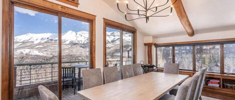 A dining area with a large table and chairs, large windows with mountain views, and a chandelier.