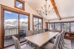Un espace repas comprenant une grande table et des chaises, de grandes fenêtres offrant une vue sur les montagnes et un lustre.