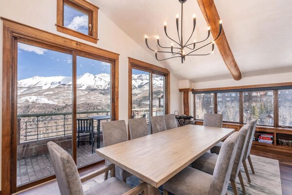 A dining area with a large table and chairs, large windows with mountain views, and a chandelier.