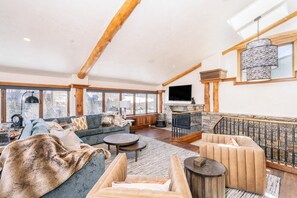 A spacious living room with a fireplace, large windows, and a stone wall.