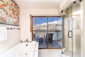 Une salle de bain avec une baignoire, une douche à parois de verre et une vue sur un paysage montagneux enneigé.