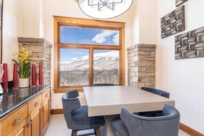 A dining area with a table and chairs, a window with a mountain view, stone walls, and a wooden cabinet.