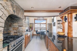 A kitchen with a stone arch, a gas stove, wooden cabinets, and a view through a window.