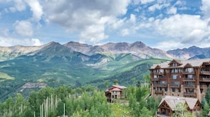 Un chalet à étages, entouré de montagnes et de verdure.