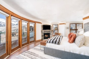 Une chambre avec une cheminée, un lit, un canapé et une vue sur un paysage enneigé, visible à travers de grandes fenêtres.