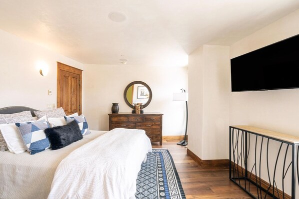 A bedroom with a bed, dresser, mirror, and a TV mounted on the wall.