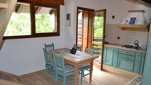 A kitchen with a wooden table and chairs, a stove, and a window overlooking greenery. - Sasso Rosso Apartment with Alps View (Folgarida)