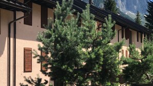 A building with a sloped roof and wooden shutters, surrounded by trees and mountains in the background. - Sasso Rosso Apartment with Alps View (Folgarida)