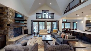 A spacious living area with a stone fireplace, a large sofa set, and a dining area with a high ceiling and large windows. - Family Fun Lodge with Access to Exclusive Golf (Bend)
