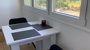 A room with a white table, two black chairs, and a view of a green landscape through large windows. - Vacation Apartment K1213 with a View of the Baltic Sea (Schönberg OT Holm)