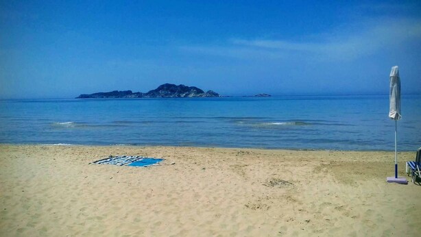 Ein Strand mit sandigem Ufer, einem blauen Handtuch und einem Strandsonnenschirm.