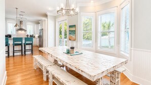 A spacious kitchen with a large wooden table, bar stools, and a view of the outdoors through large windows. - HUGE % OFF, Private Pool | 6 Bikes ☀️129 Reviews | Gulf Views | Seagrove 30A ☀️Beach Gear (Santa Rosa Beach)