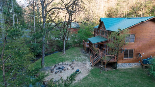 Une cabane dotée d’une terrasse, entourée d’arbres et comprenant un petit espace aménagé pour faire un feu de camp.