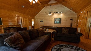 Un intérieur de chalet chaleureux avec des murs en bois, une table de billard, des canapés en cuir et un ventilateur de plafond.