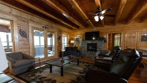 L’intérieur d’une cabane en rondins, avec une cheminée, des canapés en cuir, une table basse et un ventilateur de plafond.