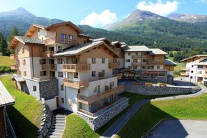 Een hotel met meerdere verdiepingen, balkons, een gevel van natuursteen en een bergachtig landschap op de achtergrond.