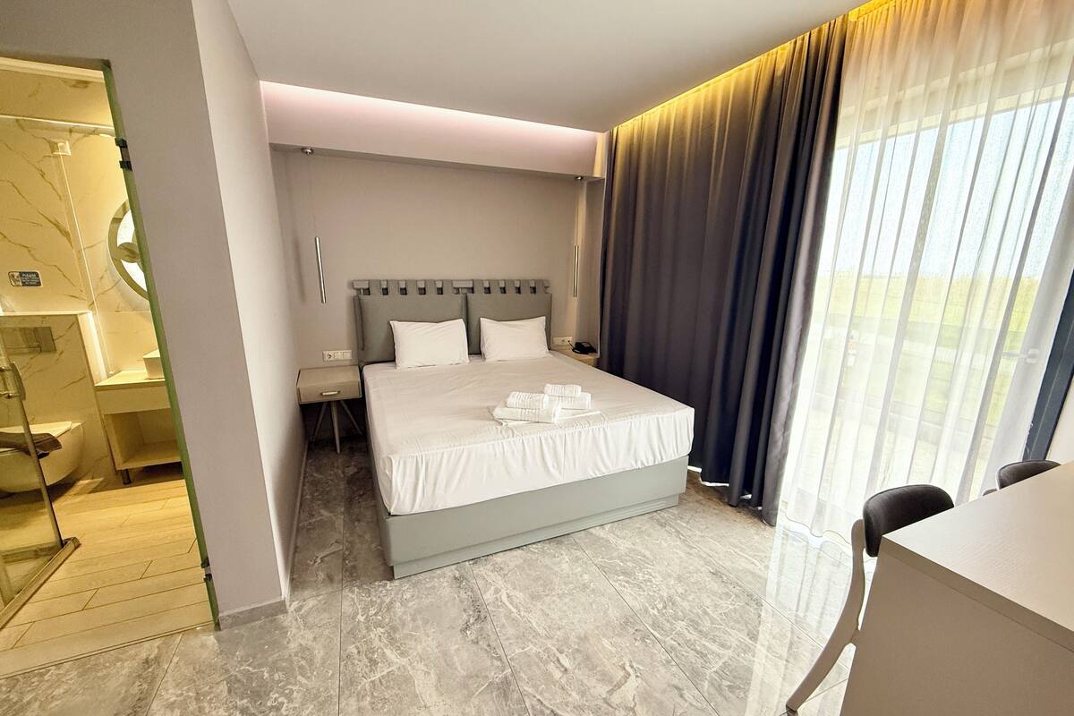 Habitación de hotel moderna con una cama grande, un escritorio y un baño con cabina de ducha de vidrio.