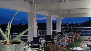 Une terrasse avec des chaises et des tables en osier, une balançoire suspendue et une vue sur les montagnes au crépuscule.