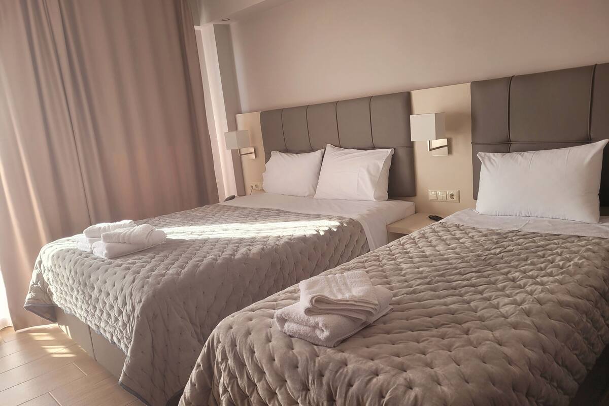 Habitación de hotel con dos camas, cada una con cabecera, mesitas de noche y lámparas.